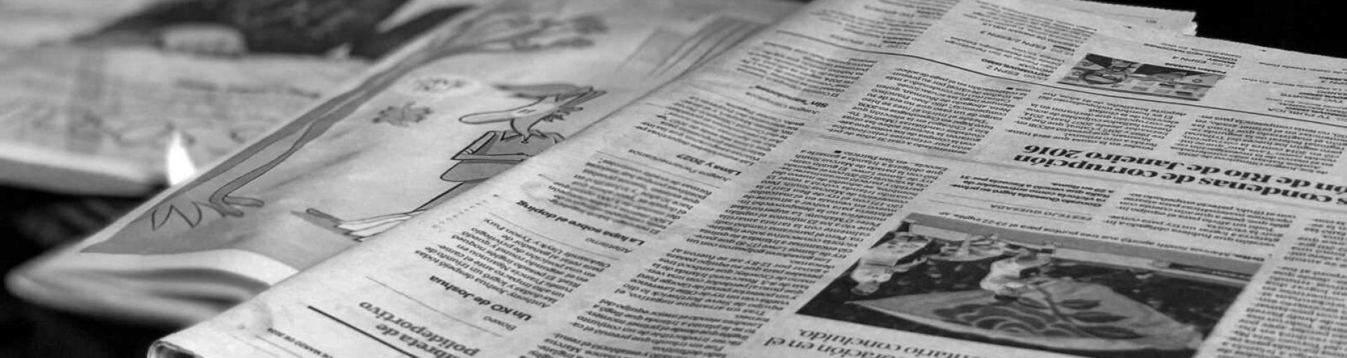 Black and white close-up image of newspapers laid on a table, emphasizing print media.